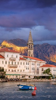 Eski Perast kasabası, Karadağ, gün batımında. Kırmızı çatıları olan taş evler, bir kilise kulesi ve sakin sular dağlar ve güneş ışığıyla sakin bir manzara yaratır. 