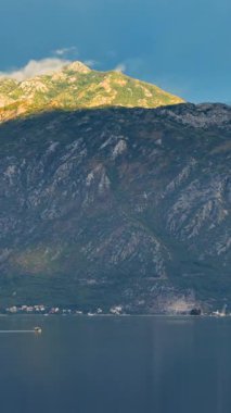 Kotor Körfezi 'nde, sabah güneşleri bulutları delip geçer, etrafındaki dağlara altın bir parıltı saçar. Görkemli bir yolcu gemisi körfeze giriyor, limana doğru süzülüyor, sakin bir manzara yaratıyor.