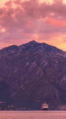 Huzurlu bir gündoğumu Kotor Körfezi 'ni sıcak renklerde yıkar, yükselen dağların üzerinde hafif bir parıltı bırakır. Karadağ 'ın engebeli manzarasının sessiz görkemini yansıtan bir yolcu gemisi zarifçe süzülüyor