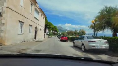 Split, Hırvatistan - Eylül 06 2024: Hırvatistan 'ın Split kenti yakınlarındaki dar bir kıyı yolu boyunca bir araba sürüyor, büyüleyici evler, yemyeşil alanlar ve yerel halkın kıyı şeridinden keyif aldığı sakin sahil manzaraları geçiyor 