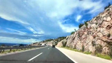 Hırvatistan 'ın Split' e giden otoyollarında kıyı boyunca uzanan virajlı otoyolu gören manzaralı bir gezinti. Adriyatik Denizi sağa doğru uzanırken engebeli tepeler sola doğru yükseliyor..