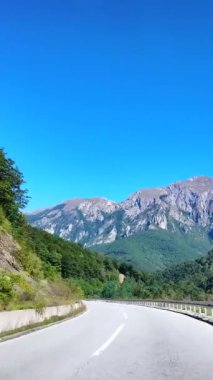 Karadağ 'ın dağlık merkez bölgesinden geçen dolambaçlı bir yolda ilerliyoruz. Bereketli yeşil ormanlar ve engebeli arazilerle çevrili yol, açık mavi gökyüzünün altındaki kayalık tepelere doğru gidiyor.