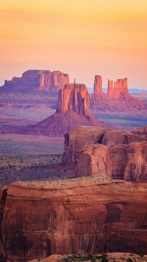 Golden sunrise paints the towering sandstone buttes and mesas of Hunts Mesa in Monument Valley tribal park, located on the Arizona-Utah border, creating a serene, otherworldly desert landscape. clipart