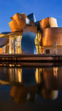 Bilbao, İspanya - 26 Eylül 2017: İspanya 'nın Bilbao kentindeki Guggenheim Müzesi' nin gece manzarası, aydınlık modern mimari, nehir yansımaları ve dolunay ile aydınlık bir akşam gökyüzü.