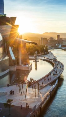 Bilbao, İspanya - 26 Eylül 2017: Bilbao 'daki Guggenheim Müzesi' nin günbatımı manzarası, modern metalik bir bina, bir örümcek heykeli, bir nehir geçidi ve yürüyen insanlar