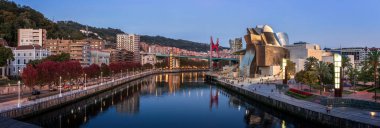 Bilbao, İspanya - 26 Eylül 2017: Modern mimarinin bir başyapıtı olan Bilbao 'nun Guggenheim Müzesi, canlı sokaklar ve kırmızı La Salve Köprüsü ile çevrili Nervion Nehri' ni yansıtıyor.