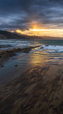 Dramatic sunset over The Flysch in Zumaia at Itzurun Beach, Northern Spain, showcasing rugged cliffs and waves, a 