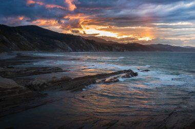 Dramatic sunset over The Flysch in Zumaia at Itzurun Beach, Northern Spain, showcasing rugged cliffs and waves, a 