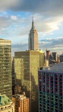 Manhattan, New York şehrinin canlı bir manzarası. Parçalı bulutlu gökyüzünün altında, altın saat batımında modern gökdelenleri var..