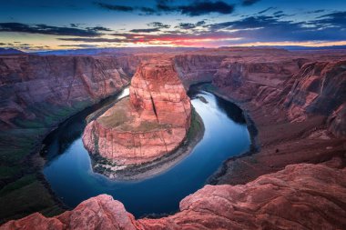 Gün batımında Horseshoe Bend Colorado Nehri 'nin kırmızı kumtaşı uçurumlarında renkli bir gökyüzü altında kıvrıldığını gösteriyor. Arizona, Page yakınlarında nefes kesici bir doğa harikası. Fotoğrafçılık için mükemmel..
