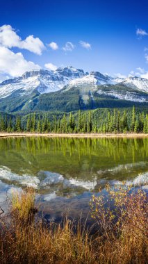 Kanada 'daki Rampart Pond' da karlı dağların ve yemyeşil ormanların berrak yansımaları. Kanada Kayalıkları 'nın kalbinde dingin ve nefes kesici bir manzara.