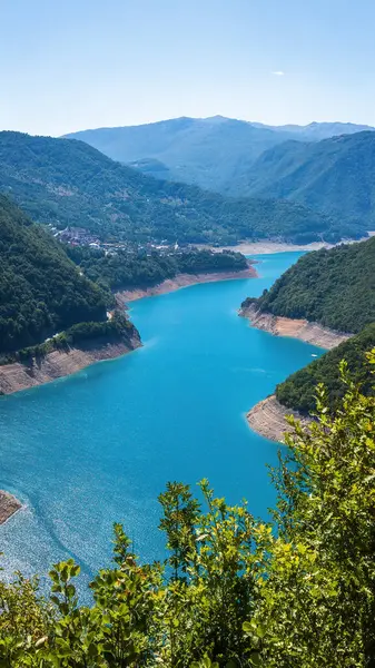 Karadağ 'daki Piva Gölü parlak turkuaz suyla parıldıyor, berrak bir yaz gökyüzü altında yemyeşil dağların arasından süzülerek nefes kesici bir doğal manzara yaratıyor..