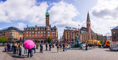  Kopenhag 'ın merkezindeki canlı şehir meydanı tarihi mimari, dekoratif bir çeşme, turistler ve bulutlu mavi bir gökyüzü..