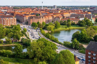 Kurtarıcımız Kilisesi 'nin tepesinden alınan Kopenhag' ın panoramik manzarası sıcak bir akşam gökyüzü altında tarihi çatılar, modern binalar ve şehir simgelerinin bir karışımını gösteriyor..