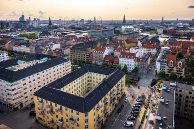Kurtarıcımız Kilisesi 'nin tepesinden alınan Kopenhag' ın panoramik manzarası sıcak bir akşam gökyüzü altında tarihi çatılar, modern binalar ve şehir simgelerinin bir karışımını gösteriyor..