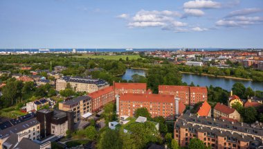 Kurtarıcımız Kilisesi 'nin tepesinden alınan Kopenhag' ın panoramik manzarası sıcak bir akşam gökyüzü altında tarihi çatılar, modern binalar ve şehir simgelerinin bir karışımını gösteriyor..