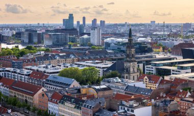 Kurtarıcımız Kilisesi 'nin tepesinden alınan Kopenhag' ın panoramik manzarası sıcak bir akşam gökyüzü altında tarihi çatılar, modern binalar ve şehir simgelerinin bir karışımını gösteriyor..