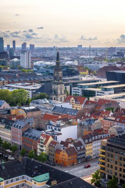 Kurtarıcımız Kilisesi 'nin tepesinden alınan Kopenhag' ın panoramik manzarası sıcak bir akşam gökyüzü altında tarihi çatılar, modern binalar ve şehir simgelerinin bir karışımını gösteriyor..