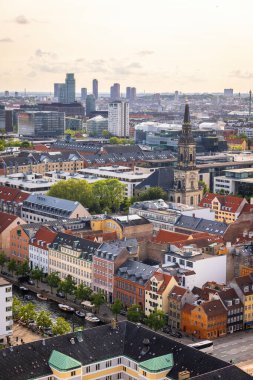 Kurtarıcımız Kilisesi 'nin tepesinden alınan Kopenhag' ın panoramik manzarası sıcak bir akşam gökyüzü altında tarihi çatılar, modern binalar ve şehir simgelerinin bir karışımını gösteriyor..