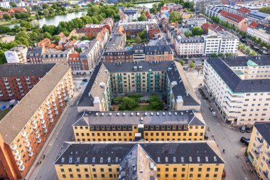 Kurtarıcımız Kilisesi 'nin tepesinden alınan Kopenhag' ın panoramik manzarası sıcak bir akşam gökyüzü altında tarihi çatılar, modern binalar ve şehir simgelerinin bir karışımını gösteriyor..