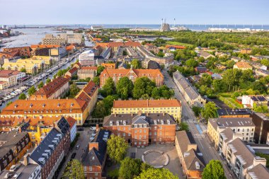 Kurtarıcımız Kilisesi 'nin tepesinden alınan Kopenhag' ın panoramik manzarası sıcak bir akşam gökyüzü altında tarihi çatılar, modern binalar ve şehir simgelerinin bir karışımını gösteriyor..