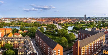 Kurtarıcımız Kilisesi 'nin tepesinden alınan Kopenhag' ın panoramik manzarası sıcak bir akşam gökyüzü altında tarihi çatılar, modern binalar ve şehir simgelerinin bir karışımını gösteriyor..