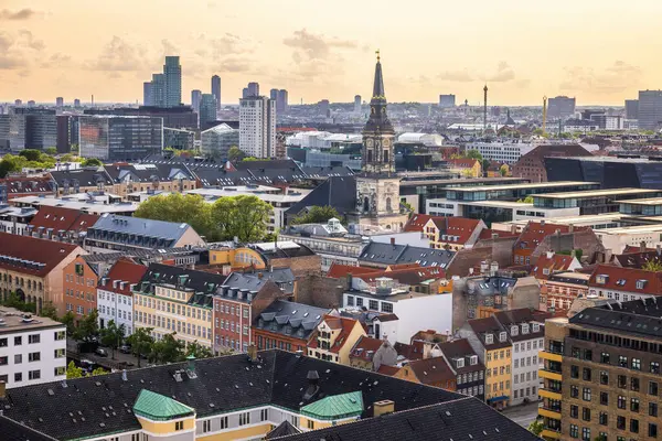 Kurtarıcımız Kilisesi 'nin tepesinden alınan Kopenhag' ın panoramik manzarası sıcak bir akşam gökyüzü altında tarihi çatılar, modern binalar ve şehir simgelerinin bir karışımını gösteriyor..