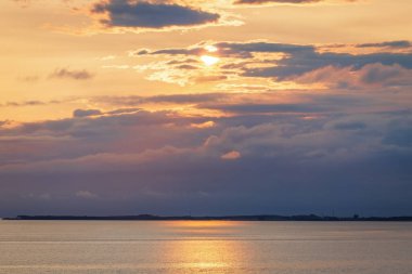 Norveç denizi üzerinde altın bir günbatımı dramatik bulutlar ve sakin su yüzeyinde parıldayan parlak yansımalarla. Huzurlu, atmosferik bir akşam sahnesi. Yolcu gemisinden görüntüle.