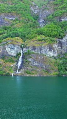 Görkemli şelaleler yemyeşil bir dağdan Norveç fiyorduna dökülüyor, bir yolcu gemisinden görülüyor. Doğal güzelliğin ve sükunetin nefes kesici bir sahnesi..