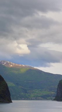 Yeşil yemyeşil tepeleri ve karla kaplı dağları olan Norveç kıyı şeridinin manzarası fiyorttan geçen bir yolcu gemisinden çekiliyor. 