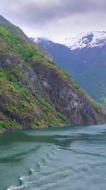 Norveç fiyortlarının sakin sularında seyreden bir geminin arkasında dalgalar yumuşak güneş ışığı altında yüzeyde ritmik ve yansıtıcı bir desen oluşturuyor..