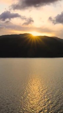 Norveç denizi üzerinde gün batımı, dramatik bulutlar ve sakin su yüzeyinde parıldayan yansımalarla. Huzurlu, atmosferik bir akşam sahnesi. Yolcu gemisinden görüntüle.