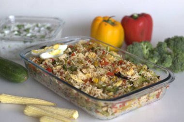 Soğuk sarımsaklı tavuk ve sebzeli pilav. Acılı sarımsak aromalı hızlı bir öğle yemeği. Basmati pilavı, sotelenmiş tavuk, bebek mısırı, dolmalık biber, havuç ve brokoli. Salatalıklı raita ile servis edilir.