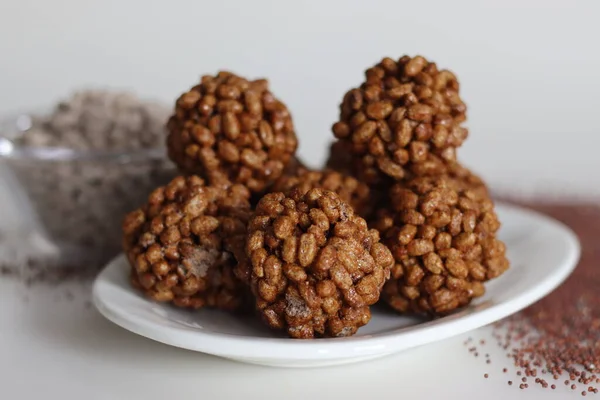 Puffed finger millet sweet ball or Ragi kurmura ladu. Sweet balls made of puffed and roasted finger millet and jaggery syrup. Shot on white background along with a bowl of puffed and roasted ragi