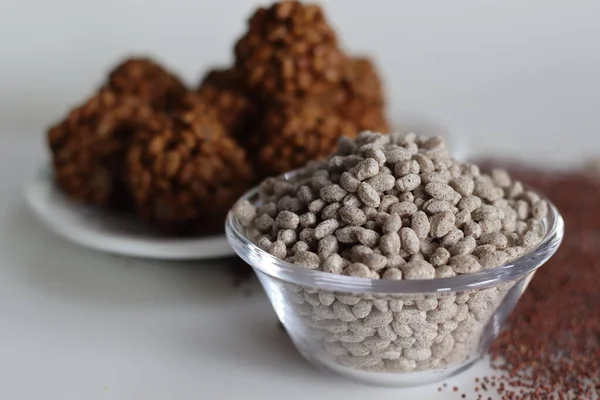 Puffed and roasted finger millet in a bowl. Shot on a white back ground along with ragi kurmura ladu made of roasted and puffed ragi.