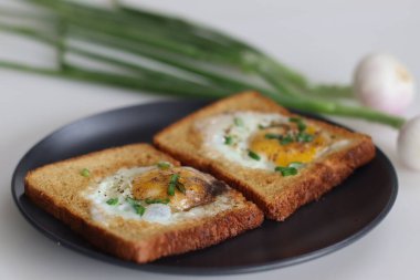 Tam on ikiden vurduk. Kızarmış yumurta tostun ortasında yapılmış bir delikte. Hızlı bir kahvaltı seçeneği, ayrıca boğa gözü tostu ya da sepette yumurta ya da delikte yumurta olarak da bilinir. Taze soğanla birlikte..