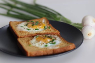 Tam on ikiden vurduk. Kızarmış yumurta tostun ortasında yapılmış bir delikte. Hızlı bir kahvaltı seçeneği, ayrıca boğa gözü tostu ya da sepette yumurta ya da delikte yumurta olarak da bilinir. Taze soğanla birlikte..