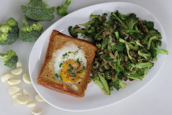 Bulls eye on bread toast. Egg fried in a hole made in the centre of toast served with stir fried broccoli. A quick breakfast option, also called bulls eye toast or egg in the basket or egg in a hole