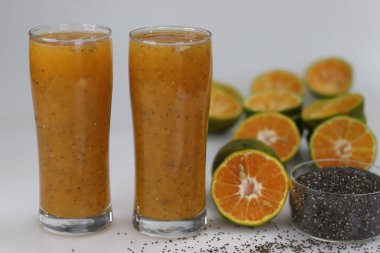 Taze sıkılmış portakal suyu ve sırılsıklam chia tohumları. Ferahlatıcı ve sağlıklı bir içecek. Şeker eklenmemiş. Beyaz arka planda, yarısı dilimlenmiş Nagpur portakalı ve chia tohumlarıyla çekilmiş.