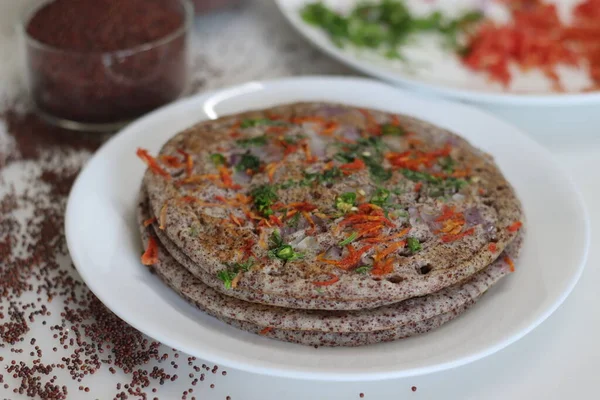 Finger millet or Ragi uthappam. Healthy pan cake made of fermented batter of finger millet and lentils. Topped with onions, carrots, coriander and green chilies. Cooked in homemade ghee.