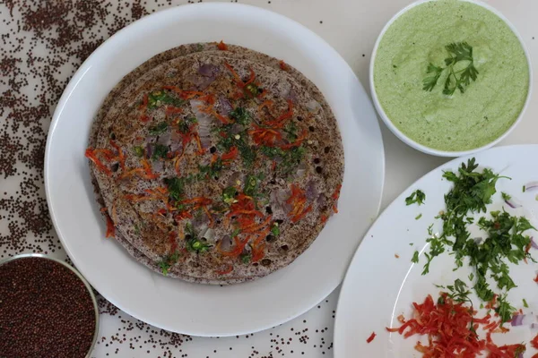 Finger millet or Ragi uthappam. Healthy pan cake made of fermented batter of finger millet and lentils. Topped with onions, carrots, coriander and green chilies. Served with coriander chutney.