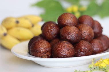 Unniyappam. Pirinç, muz, jaggery, hindistan cevizi parçaları, siyah susam tohumu ve kakule aromalı hamur tatlısı. Arka planda muz ve laburnum var.