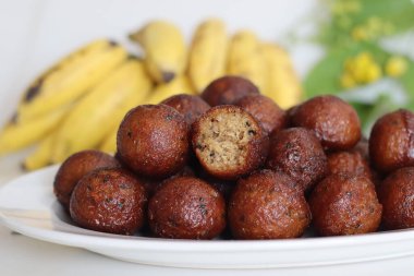 Unniyappam. Pirinç, muz, jaggery, hindistan cevizi parçaları, siyah susam tohumu ve kakule aromalı hamur tatlısı. Arka planda muz ve laburnum var.