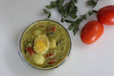 Yumurtalı köri. Hindistan cevizi sütü, domates ve soğan kullanarak Kerala usulü yumurta masala körisi. Beyaz arka planda domates ve köri yapraklarıyla çekilmiş..