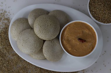 Bajra baharatlı hindistan cevizi sosuyla servis ediliyor. Fermente edilmiş siyah mercimek ve parlatılmamış inci darı hamuru tarafından yapılan buğulanmış lezzetli pirinç keki. Arka planda Bajra ile birlikte çekilmiş.