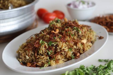 Baharatlı yahni pilavı ile hazırlanmış koyun eti biryani yanında bol miktarda karamelli soğan ve yoğurt ile marine edilmiş koyun eti. Büyük alüminyum leğen ya da uruli ile birlikte.