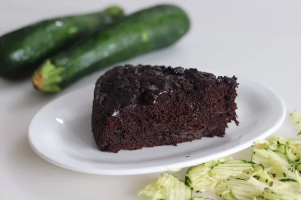 Slice of Zucchini chocolate cake. Moist double chocolate cake with grated zucchini, coco powder, chocolate and chocolate chips. Shot on white background along with zucchinis around