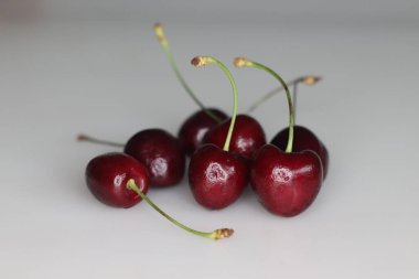 Canlı, sulu kirazlar hoş bir kümede biraraya toplanmış, yemyeşil saplara karşı zengin kırmızı renkler sergiliyorlar. Tazelik tek bir çerçevede yakalanır. Beyaz arka planda çekilmiş.