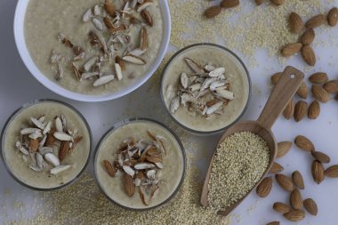 Lezzetli Proso Millet Kheer cam bir kasede, gevrek bademlerle süslenmiş, besleyici bir tatlı sergiliyor. Kasenin etrafında cömert bir altın Proso Millet yığını var. Bir de kırsal kesim var. Sağlıklı gıdalar için mükemmel bir imaj.