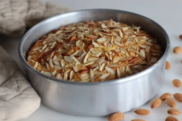 Almond buttermilk cake inside the cake tin. A delicious cake topped with a generous sprinkle of chopped almonds, perfect for tea time. Easy to make, visually appealing. Tempting treat for any occasion